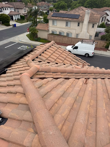 Terracotta tile roof with brown barrel tiles, solar panels, and white van in a residential area.