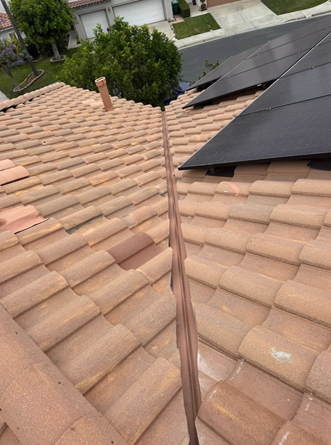 Rooftop with terracotta tiles, copper flashing, solar panels, and a chimney.