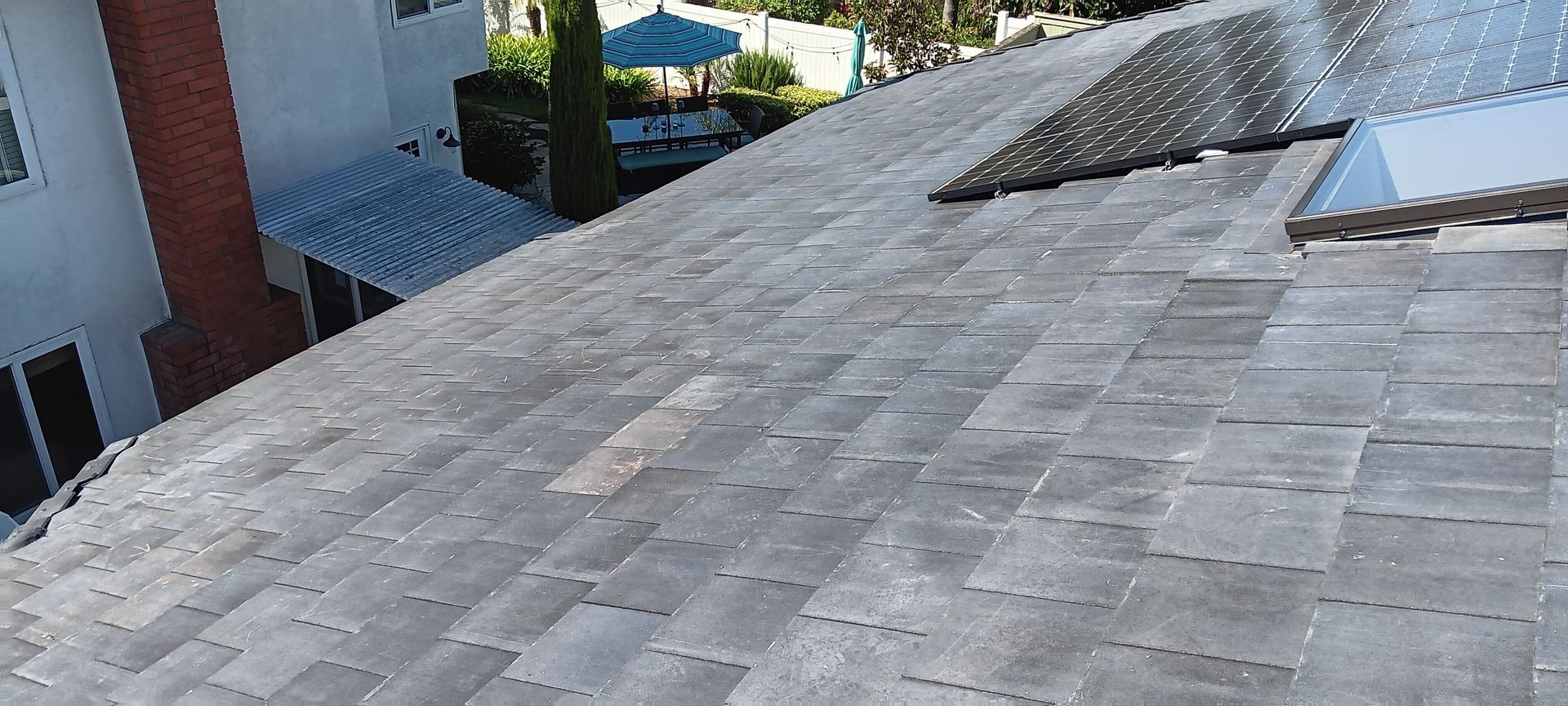 Gray roof tiles on a house, with a brick chimney and a glimpse of a gazebo in the background.