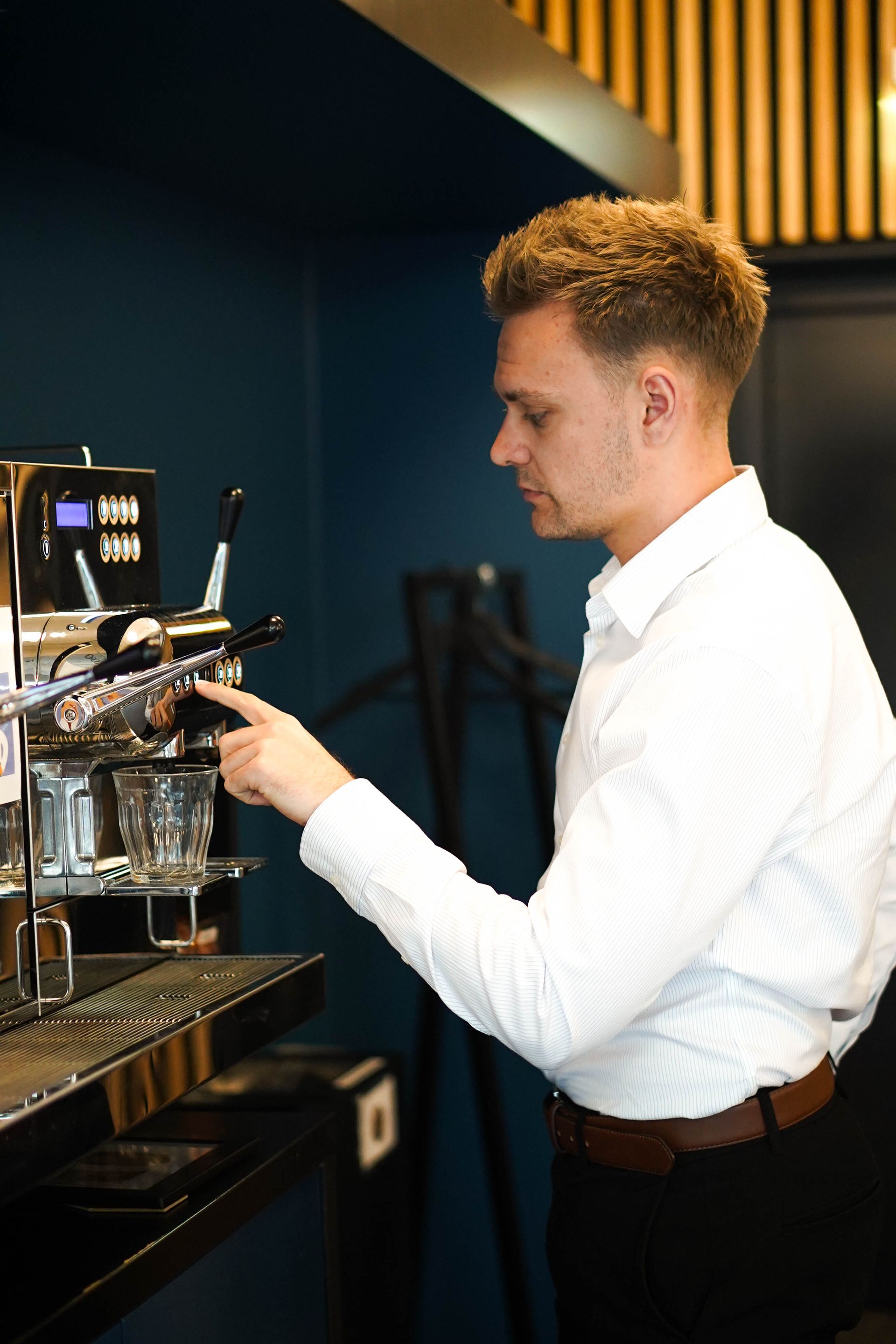 En Business Intelligence proffessionel i en hvid skjorte bruger en kaffemaskine.