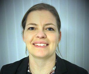 A woman in a suit and necklace is smiling for the camera.