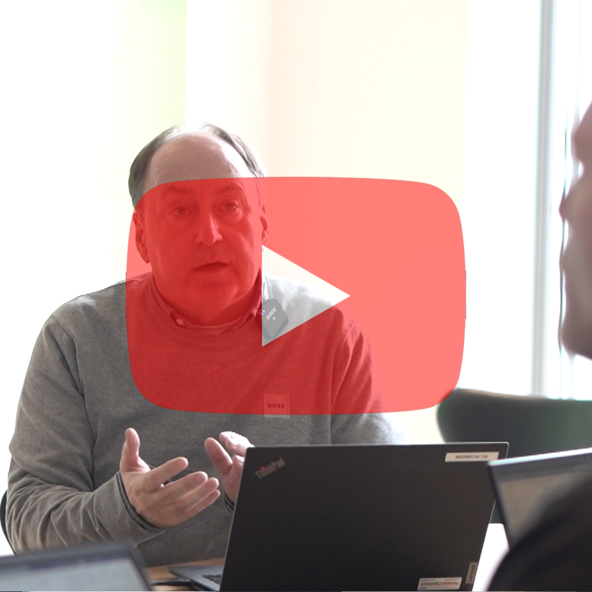 En mand, der sidder foran en bærbar computer med en rød afspilningsknap bag sig