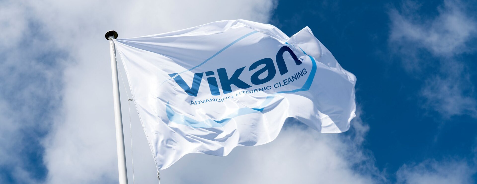 A white flag with the word vikan on it is waving in the wind.