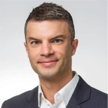 En mand i jakkesæt og hvid skjorte smiler til kameraet.