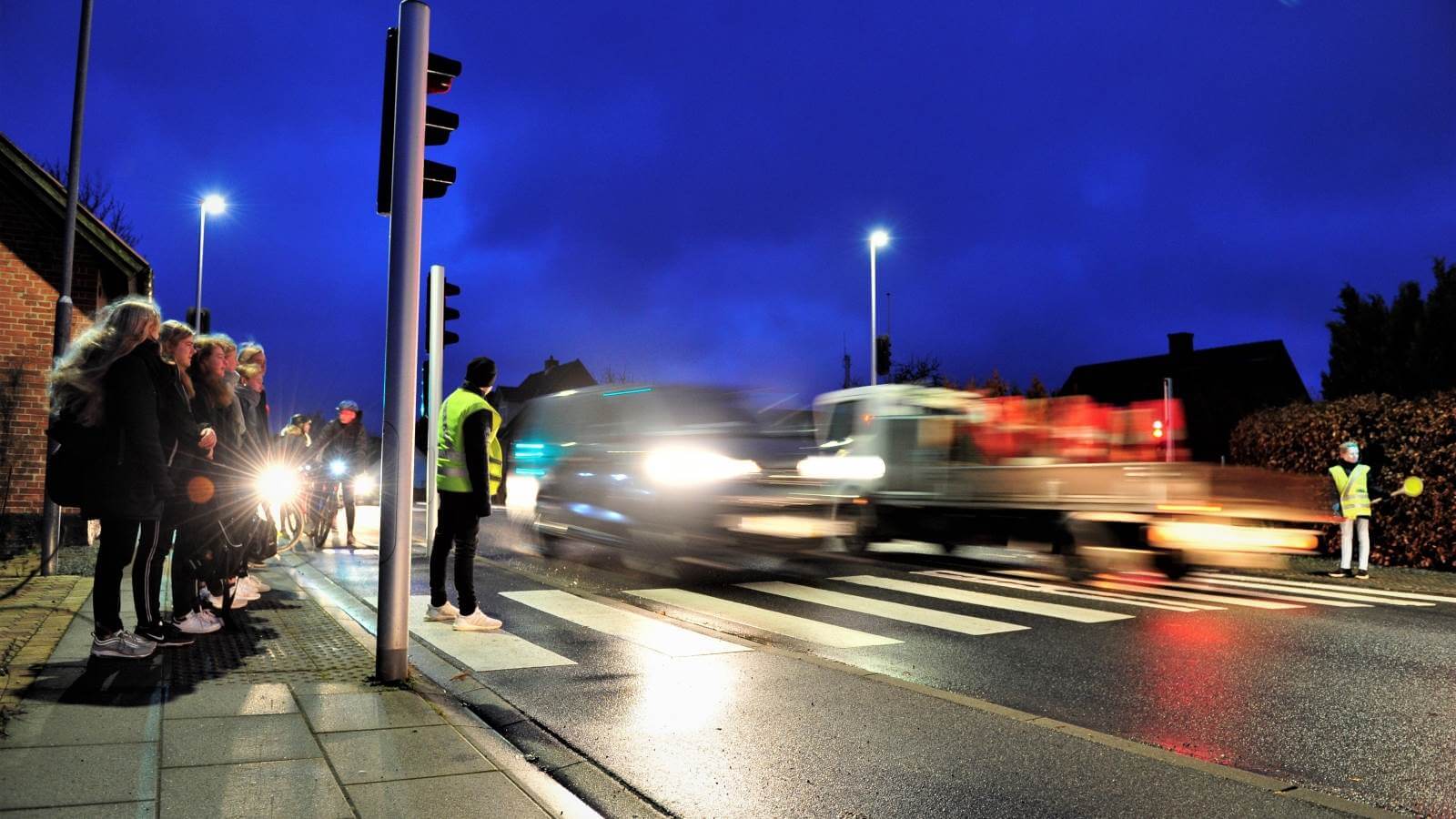 A group of people are standing on the side of the road at night.