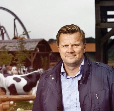 En mand i jakkesæt og hvid skjorte smiler til kameraet.