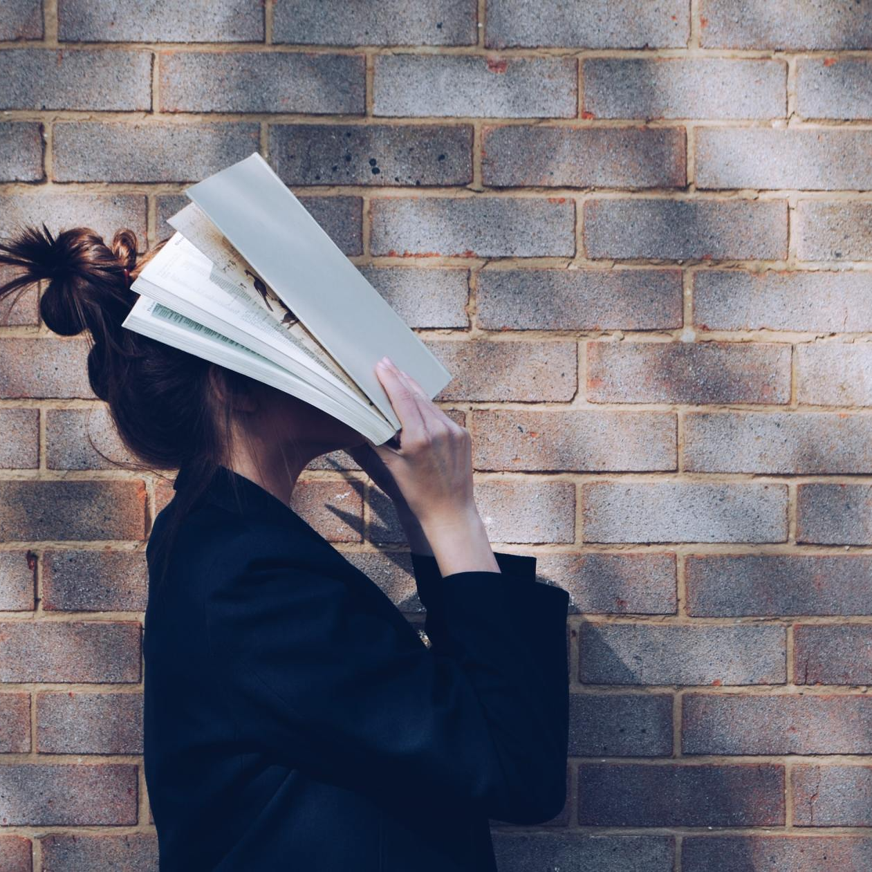 En kvinde, der dækker sit ansigt med en bog foran en murstensvæg