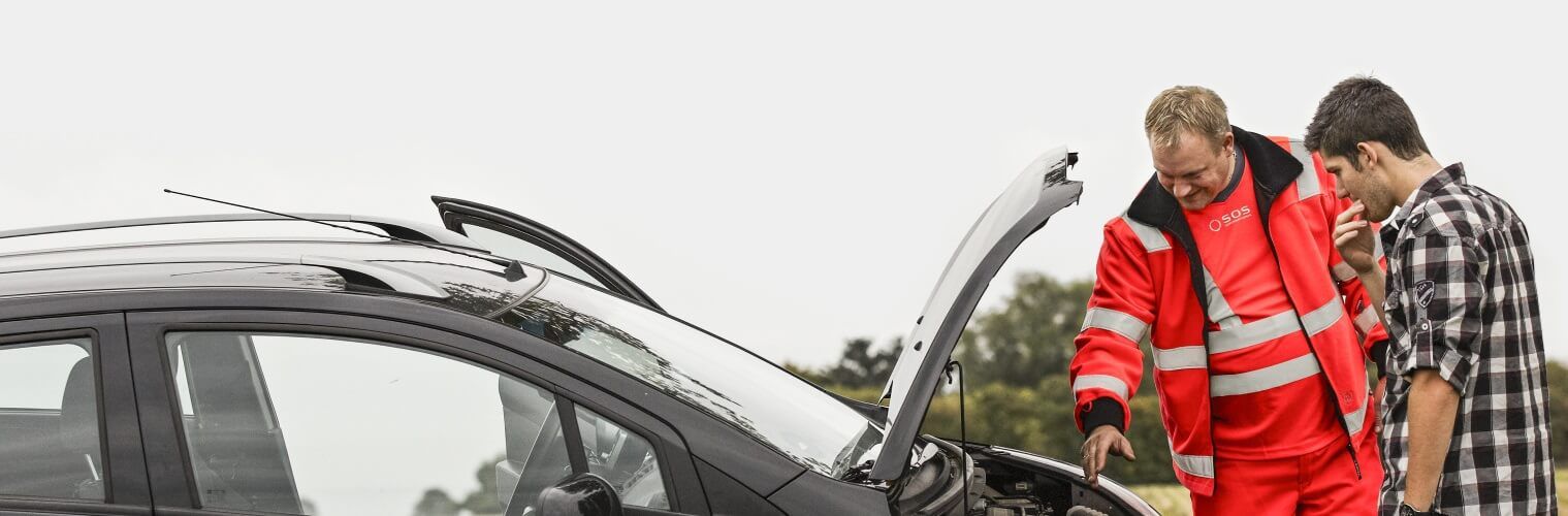 Two men are looking under the hood of a broken down car.