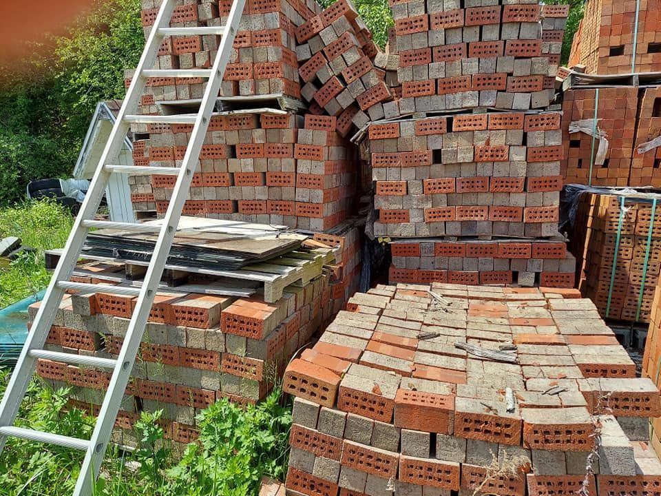 A stack of red bricks outdoors with a white ladder leaning against it.
