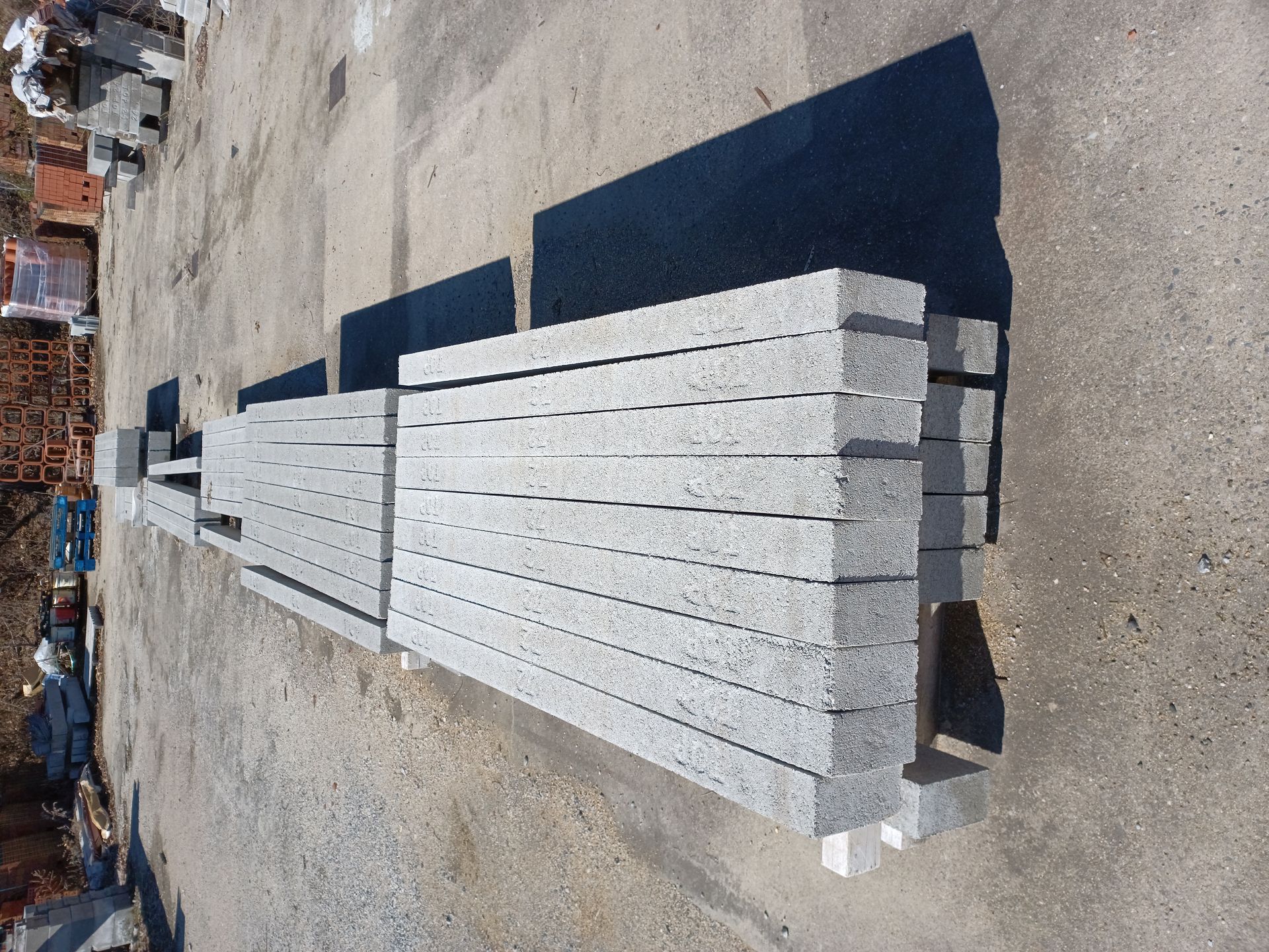 Stacked rectangular grey stone blocks arranged in rows outdoors on a concrete surface.