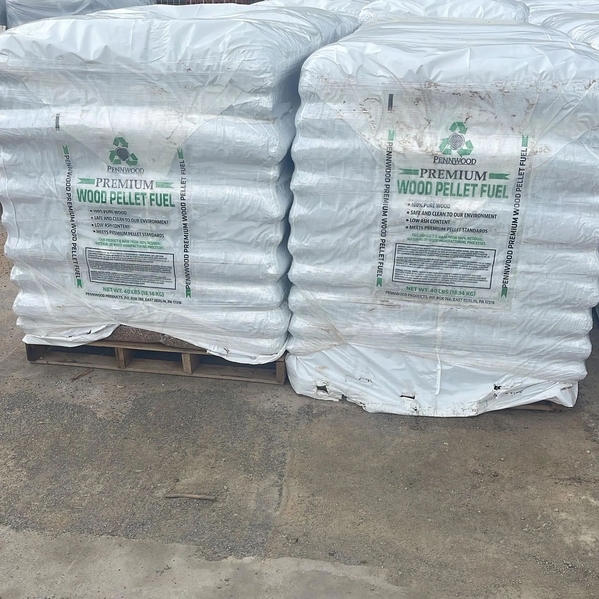 Two pallets of white-bagged premium wood pellet fuel stacked on a concrete ground.