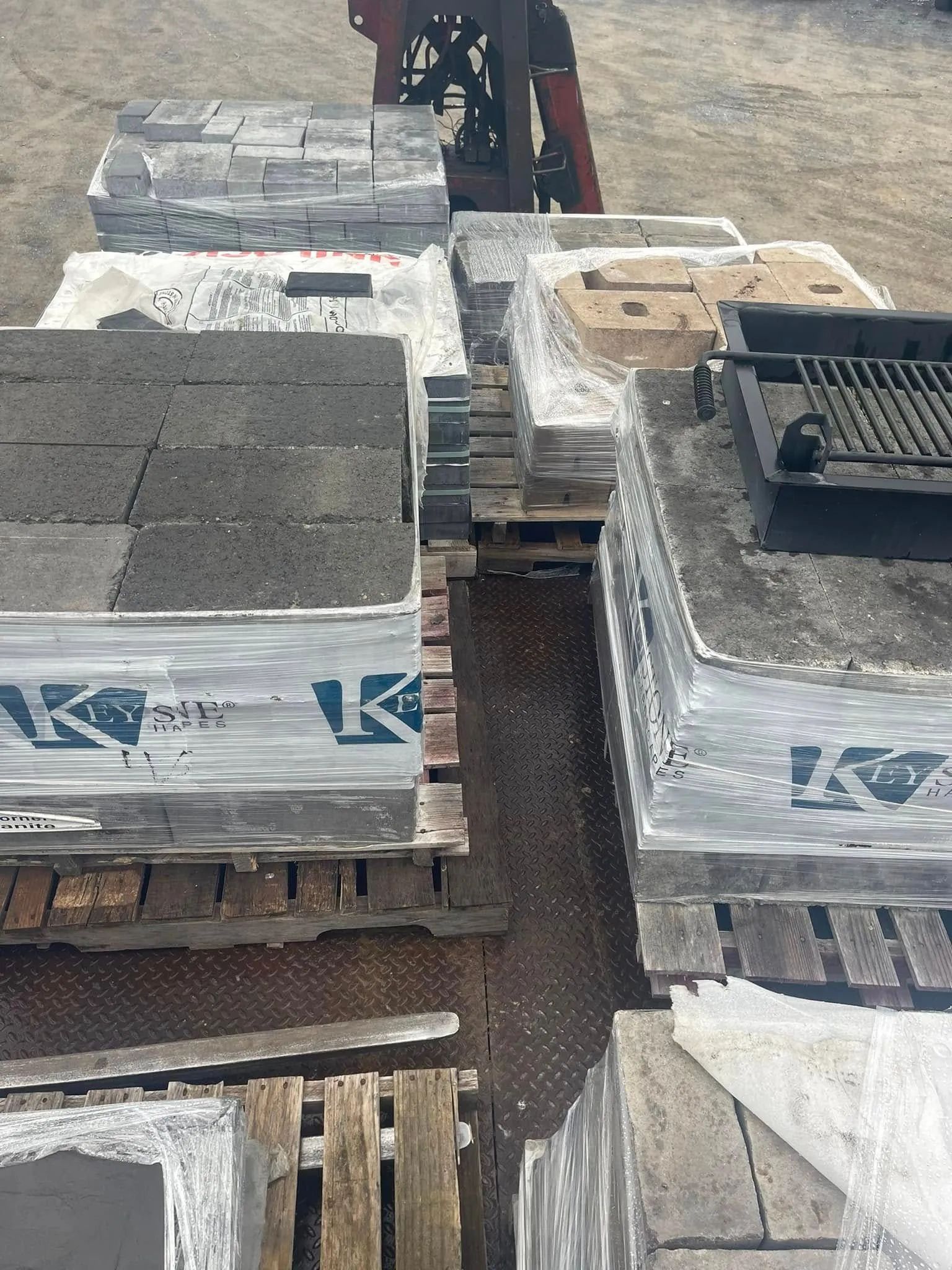 Several stacked pallets of concrete pavers and a black metal grill grate on a flatbed trailer.