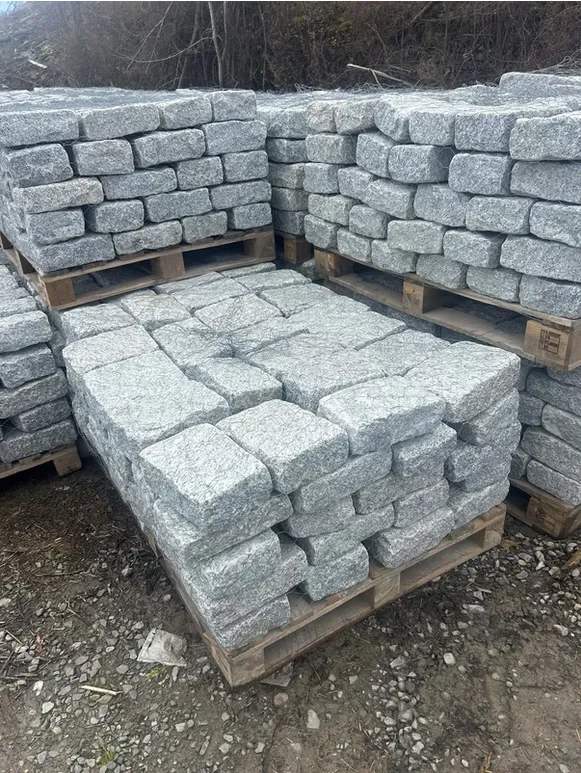 Stacked light-grey granite cobblestones arranged in neat rows on wooden pallets in an outdoor yard.
