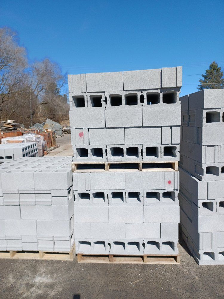 Stacked gray concrete cinder blocks on wooden pallets outdoors under a clear blue sky.