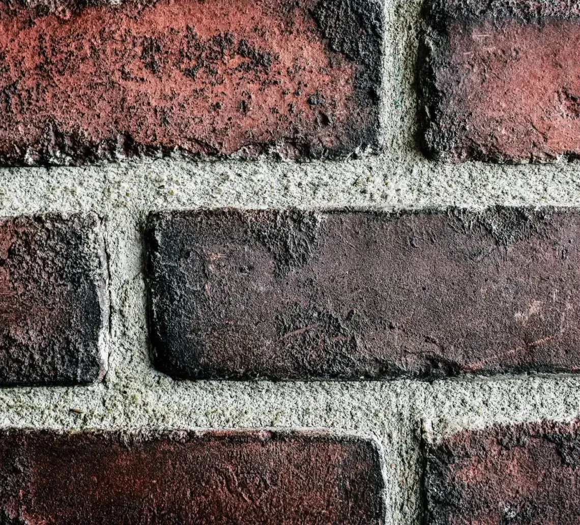 An old, weathered red brick building with a gabled wall feature and two arched, white bricked-up window or door openings.