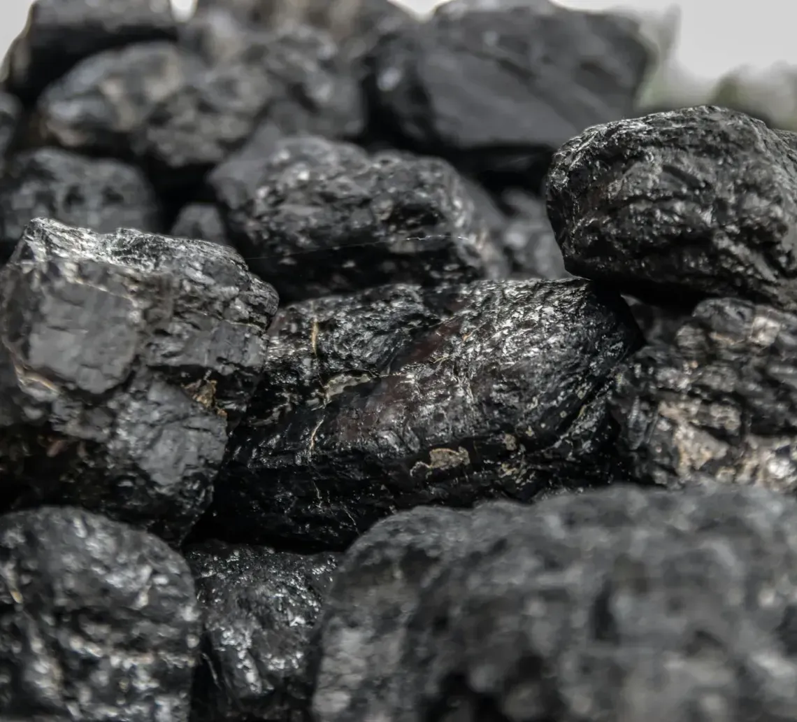 A close-up pile of rough, jagged black coal chunks with shiny, reflective surfaces.
