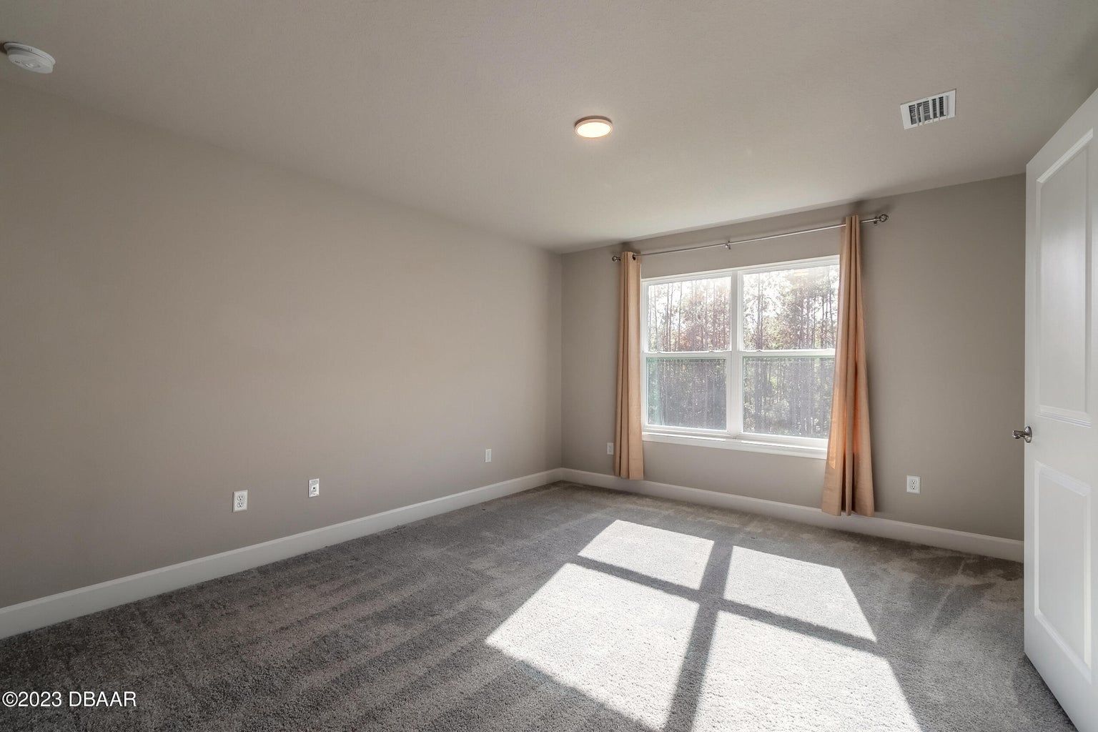 an empty bedroom with a large window and a carpeted floor .
