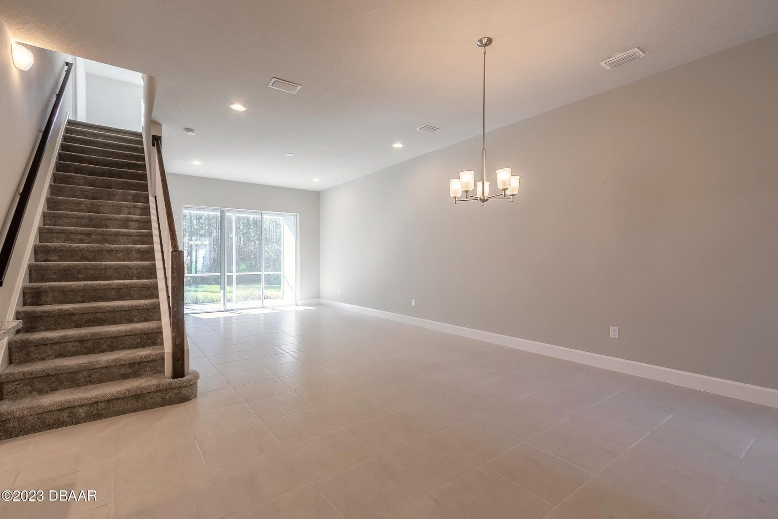 an empty living room with stairs and a chandelier