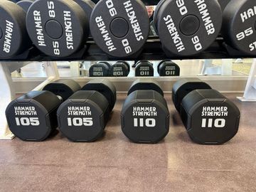 Hammer Strength dumbbells ranging from 85 to 110 pounds arranged on two gym rack shelves.