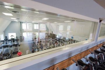 A view through a window overlooking a gym floor filled with exercise equipment, with spinning bikes in the foreground.