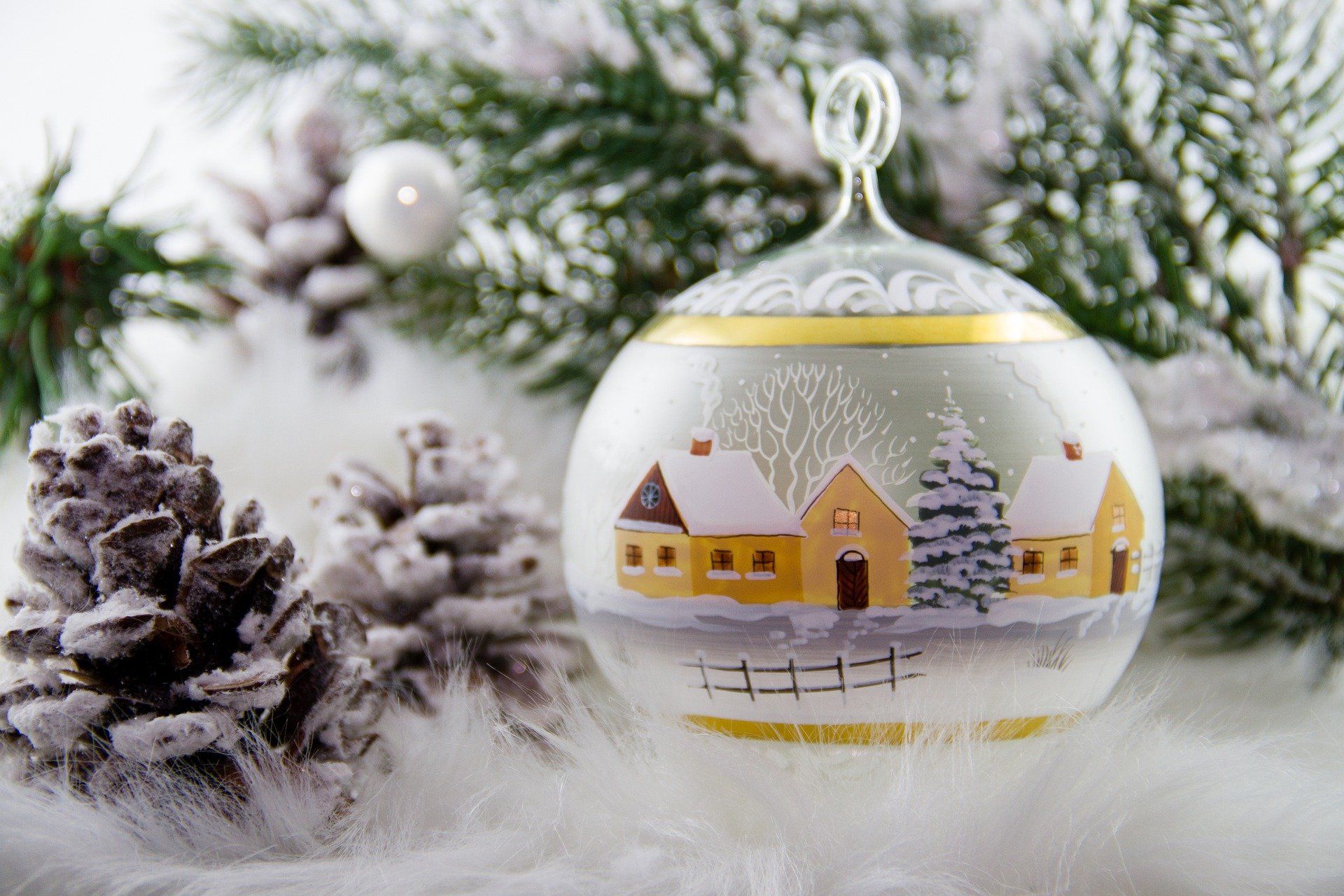 snow covered trees and a white Christmas ornament with a hand-painted house on it.