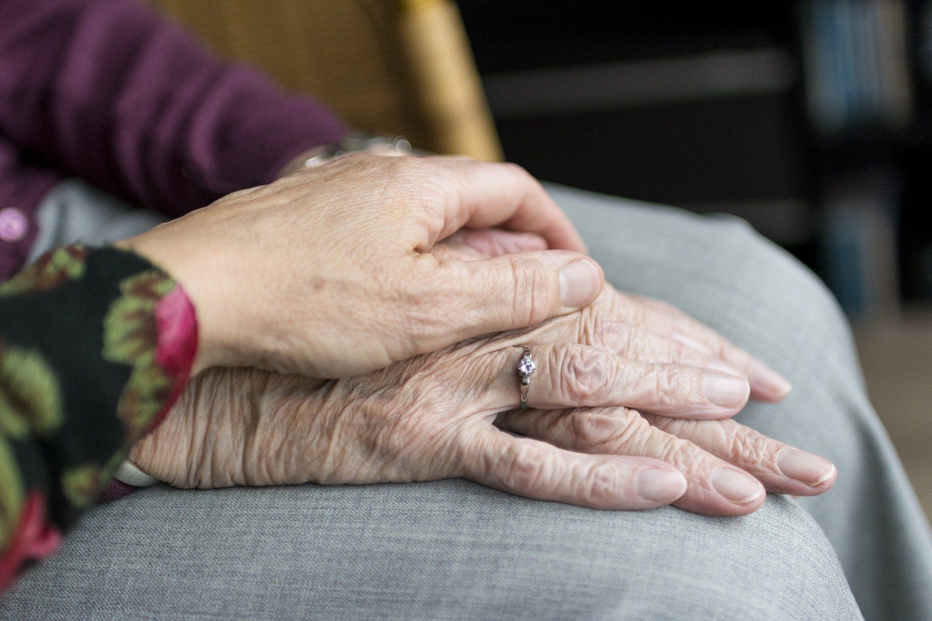 Younger hand rests atop and brings comfort to elderly hands.