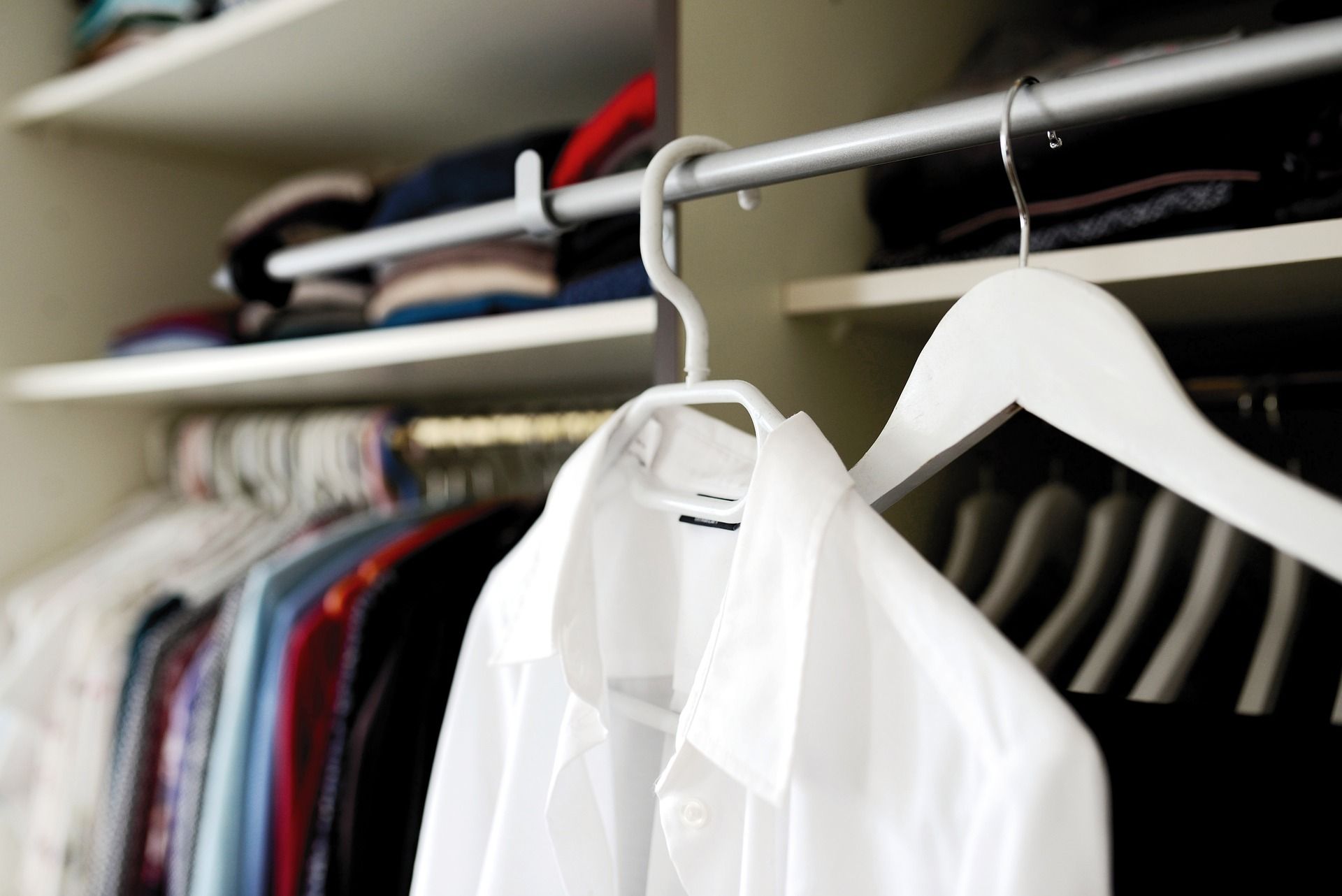 White dress shirt hangs alone on a forefront closet bar with clothing hanging on two bars behind it.