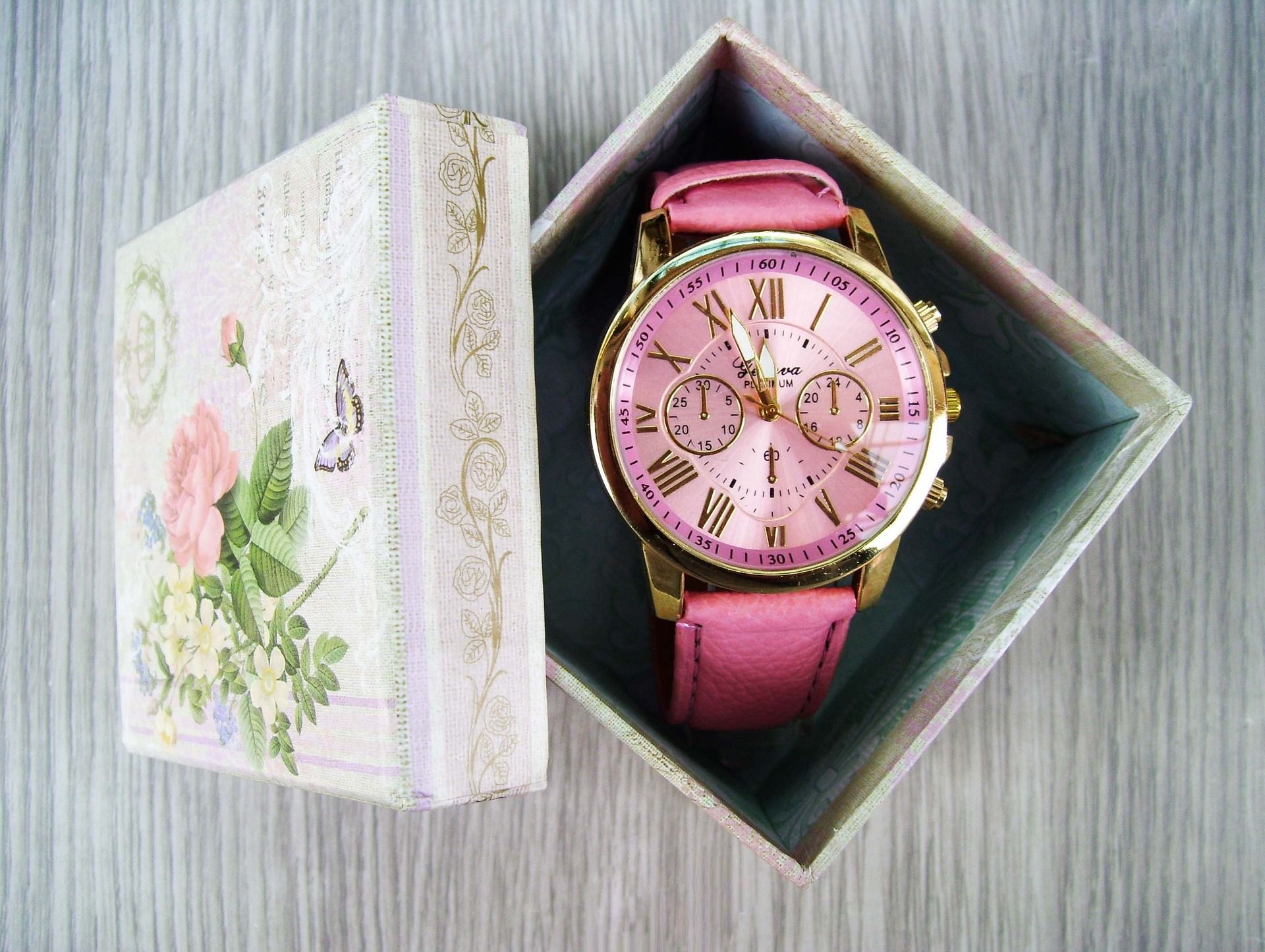 Small gift box with flowers and butterflies. Lid is open to reveal pink and gold wrist watch.