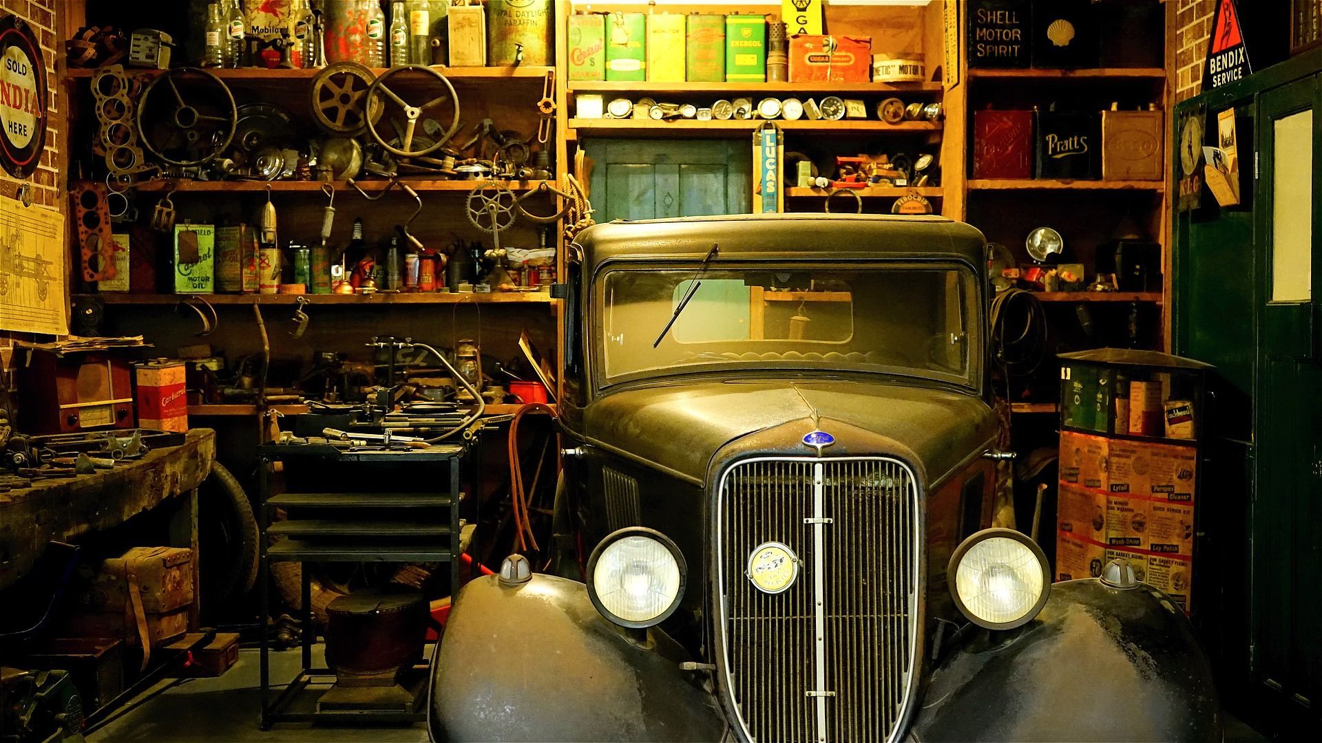Dimly lit garage with antique car, tools, hardware and shelves of chemicals with labels.