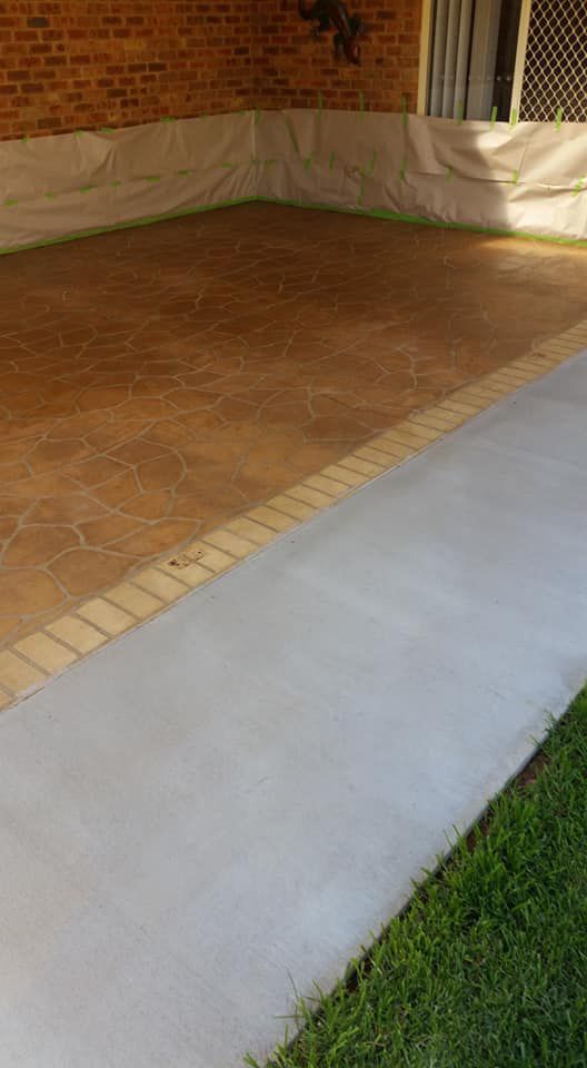 A Concrete Floor Is Being Painted In A Driveway Next To A Brick Wall — Custom Concrete Finishes In Thurgoona, NSW