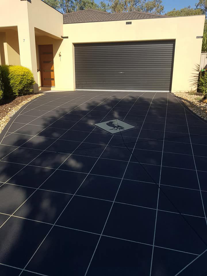 A Black Tiled Driveway Leading To A House With A Black Garage Door — Custom Concrete Finishes In Thurgoona, NSW