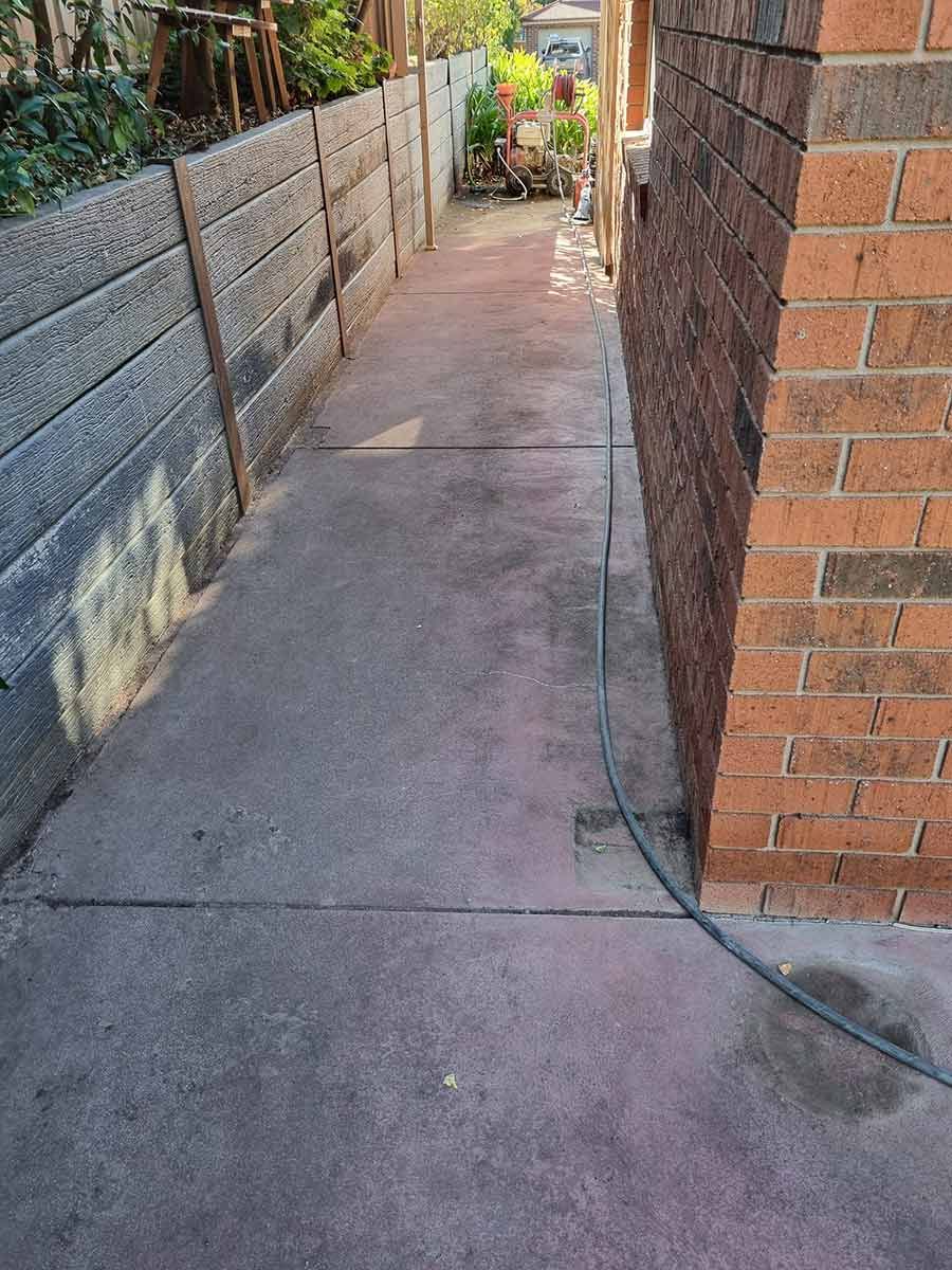 A Concrete Walkway Between Two Brick Buildings With A Hose Attached To It — Custom Concrete Finishes In Thurgoona, NSW