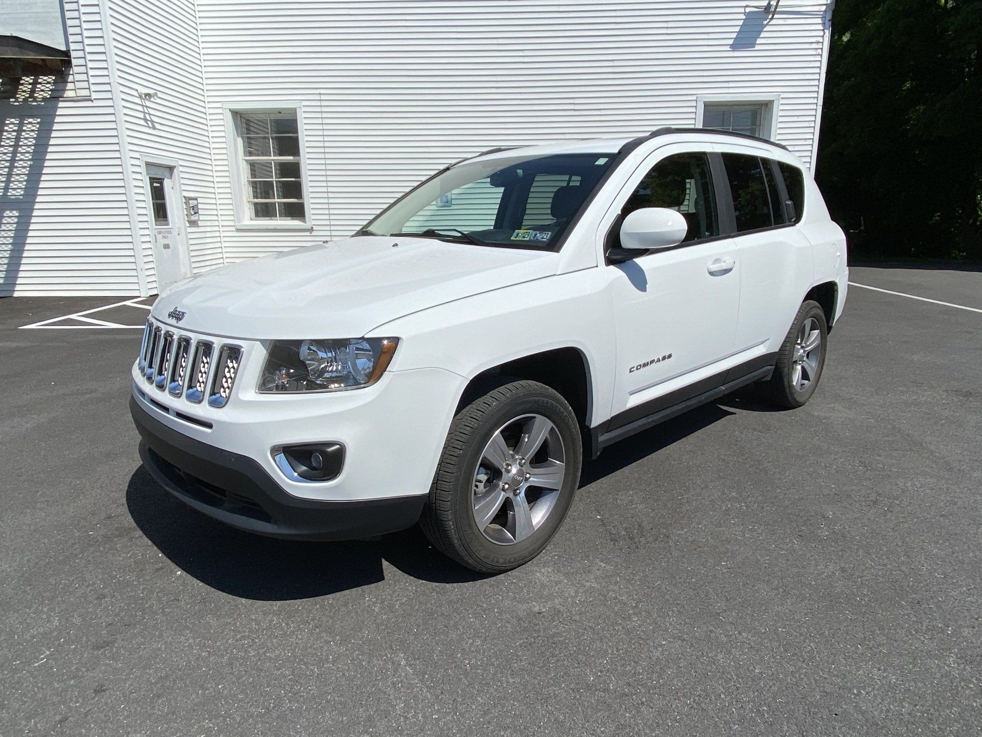 A white jeep compass is parked in front of a white building.