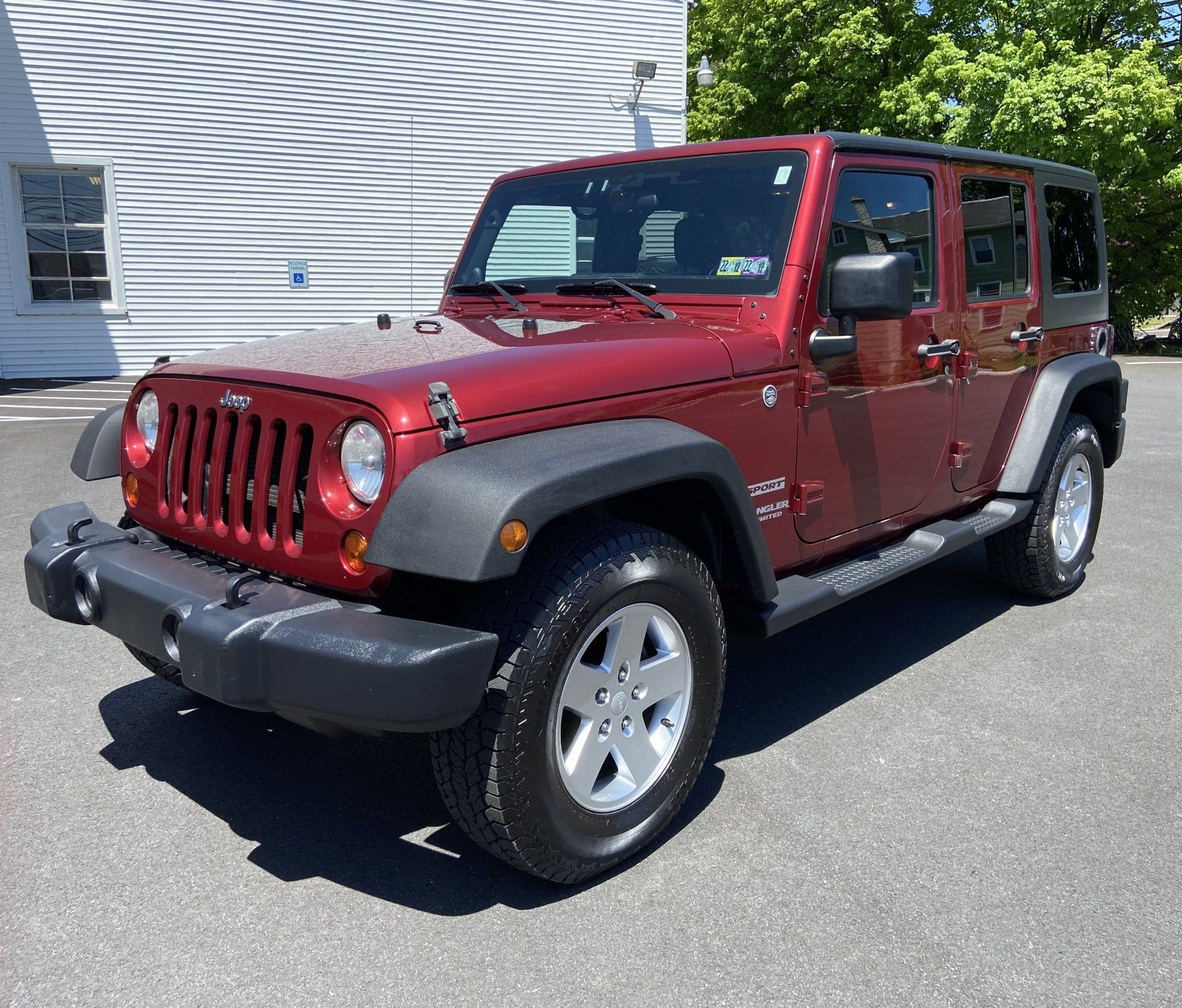 A red jeep wrangler is parked in front of a white building.