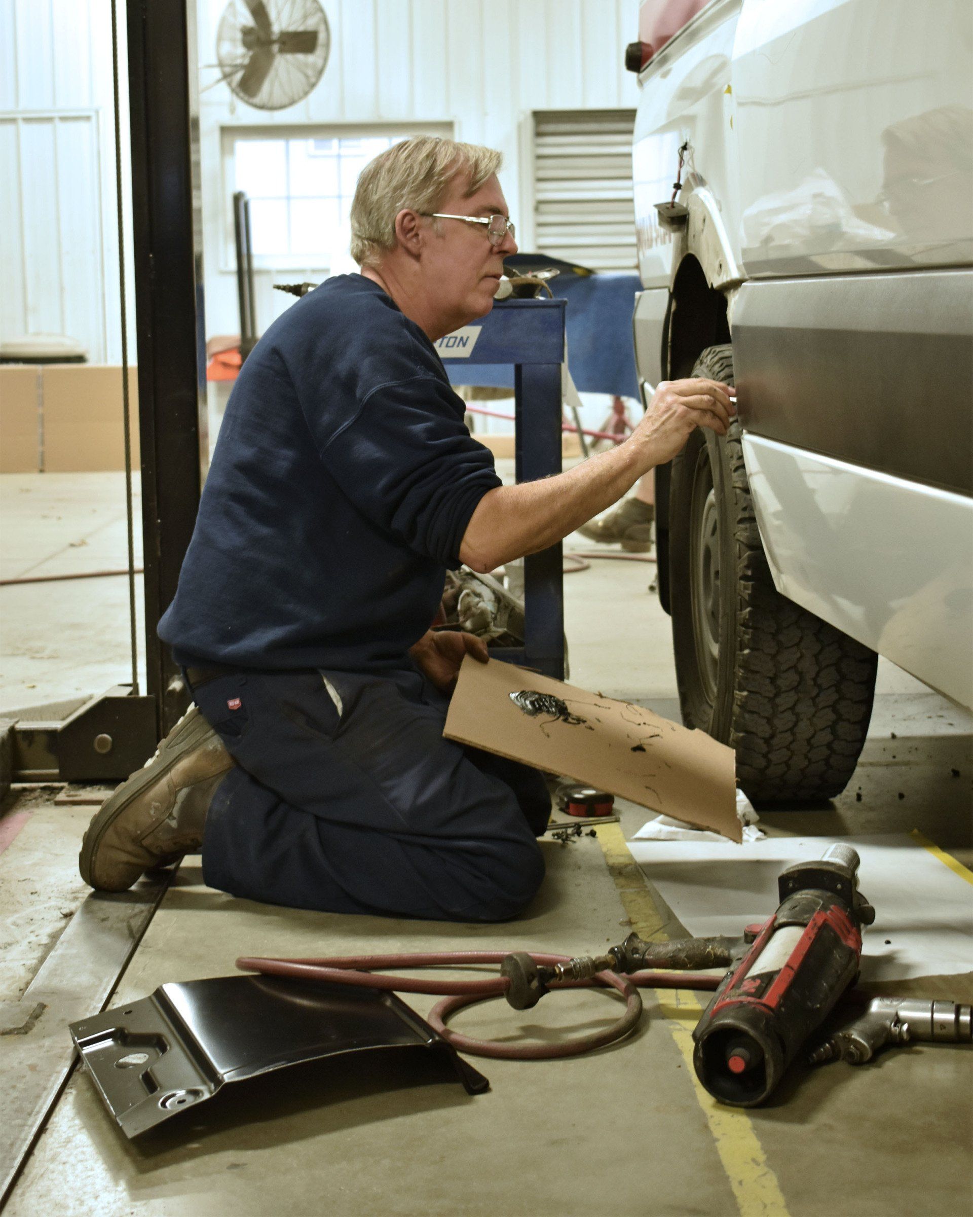 A man is kneeling down working on a car in a garage