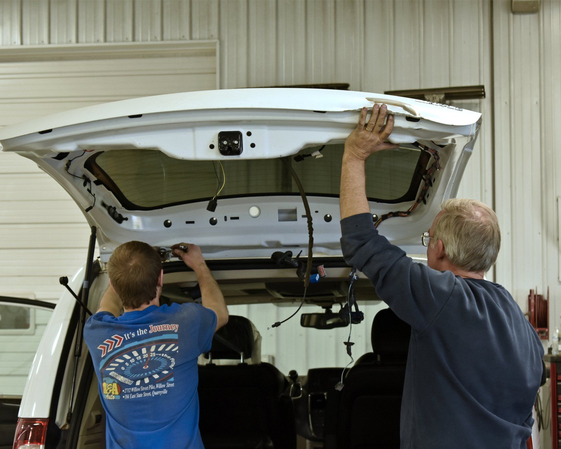 Two men are working on the trunk of a car
