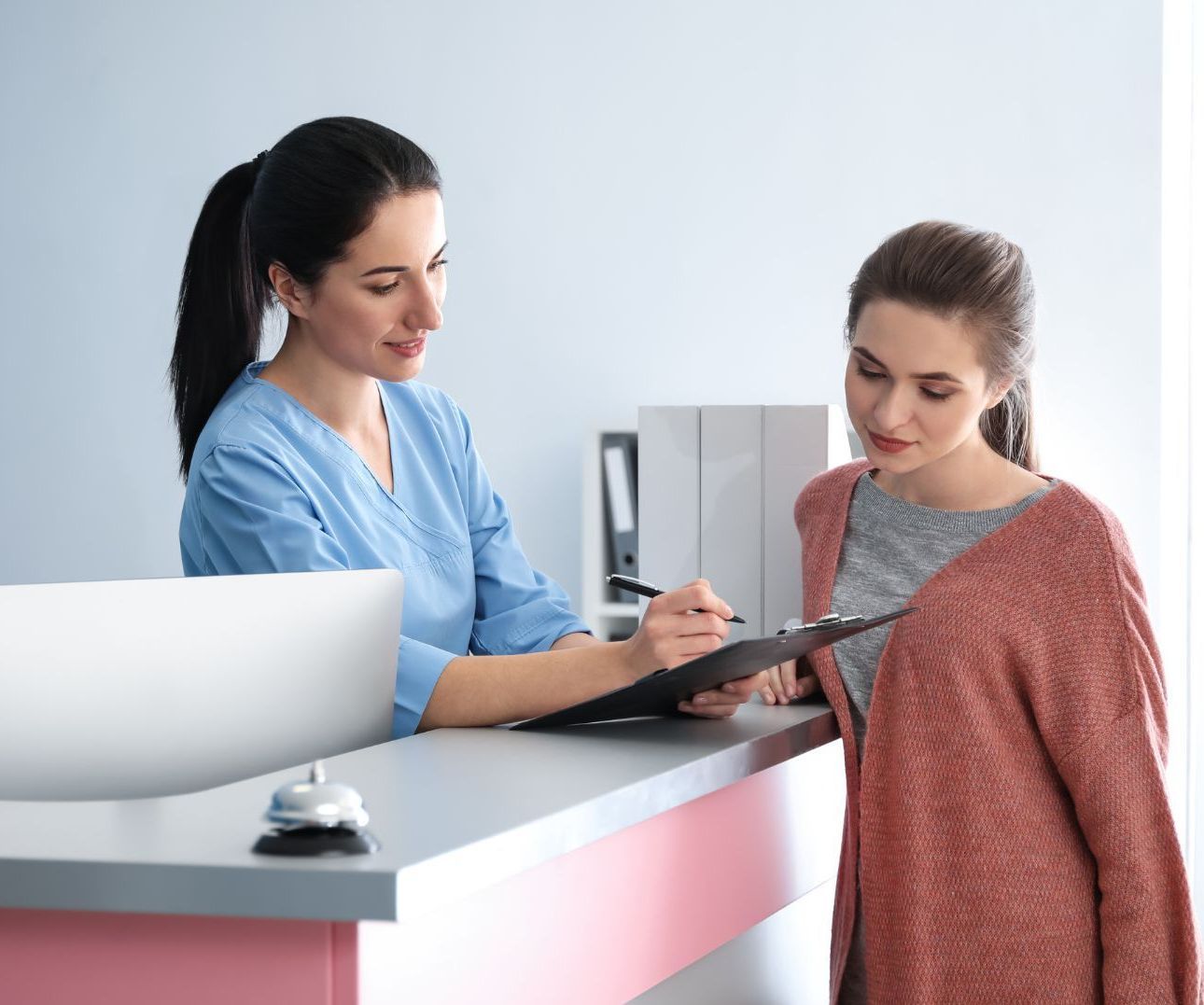 A nurse is talking to a patient at a reception desk in a hospital.