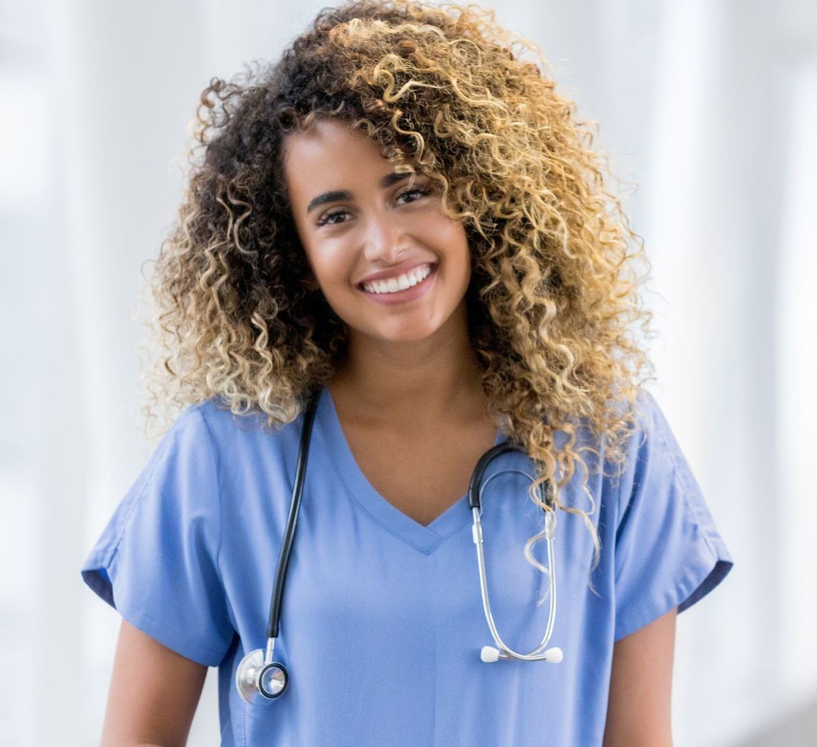 A woman with curly hair is wearing a blue scrub and a stethoscope around her neck.