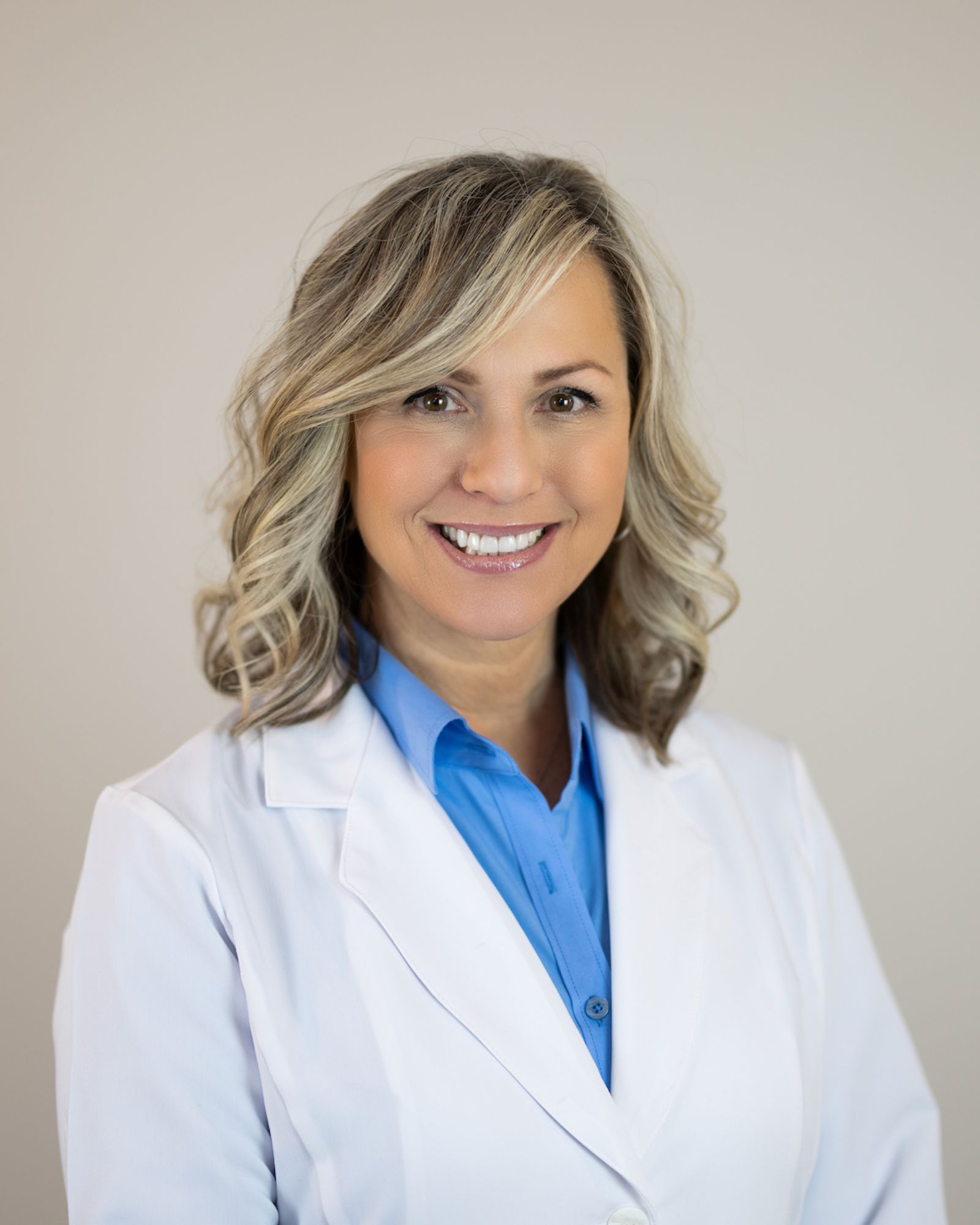 A woman in a white coat and blue shirt is smiling for the camera.