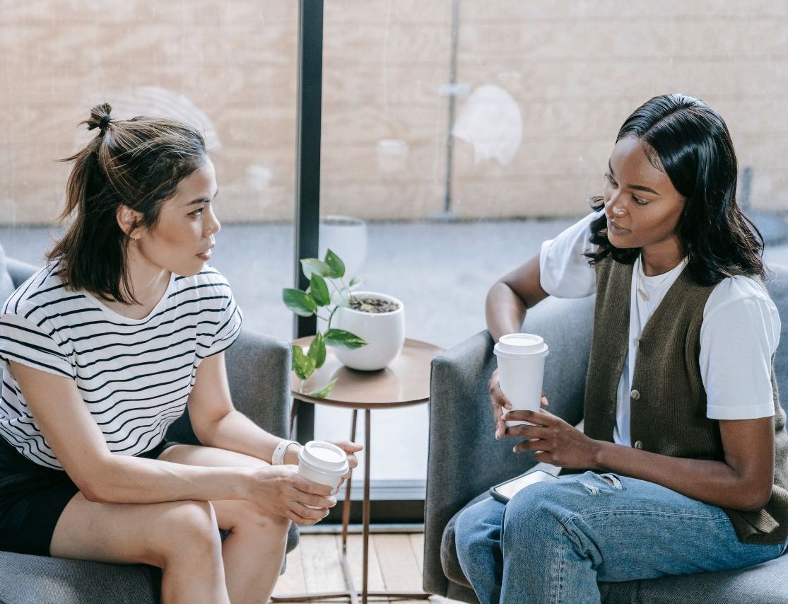 Two women are sitting on a couch talking to each other.