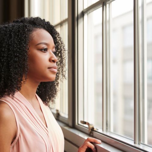 A woman with curly hair is looking out of a window.