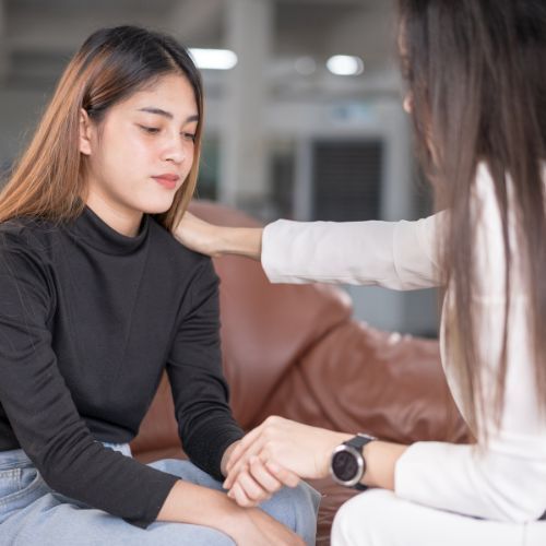 A woman is comforting another woman who is sitting on a couch.