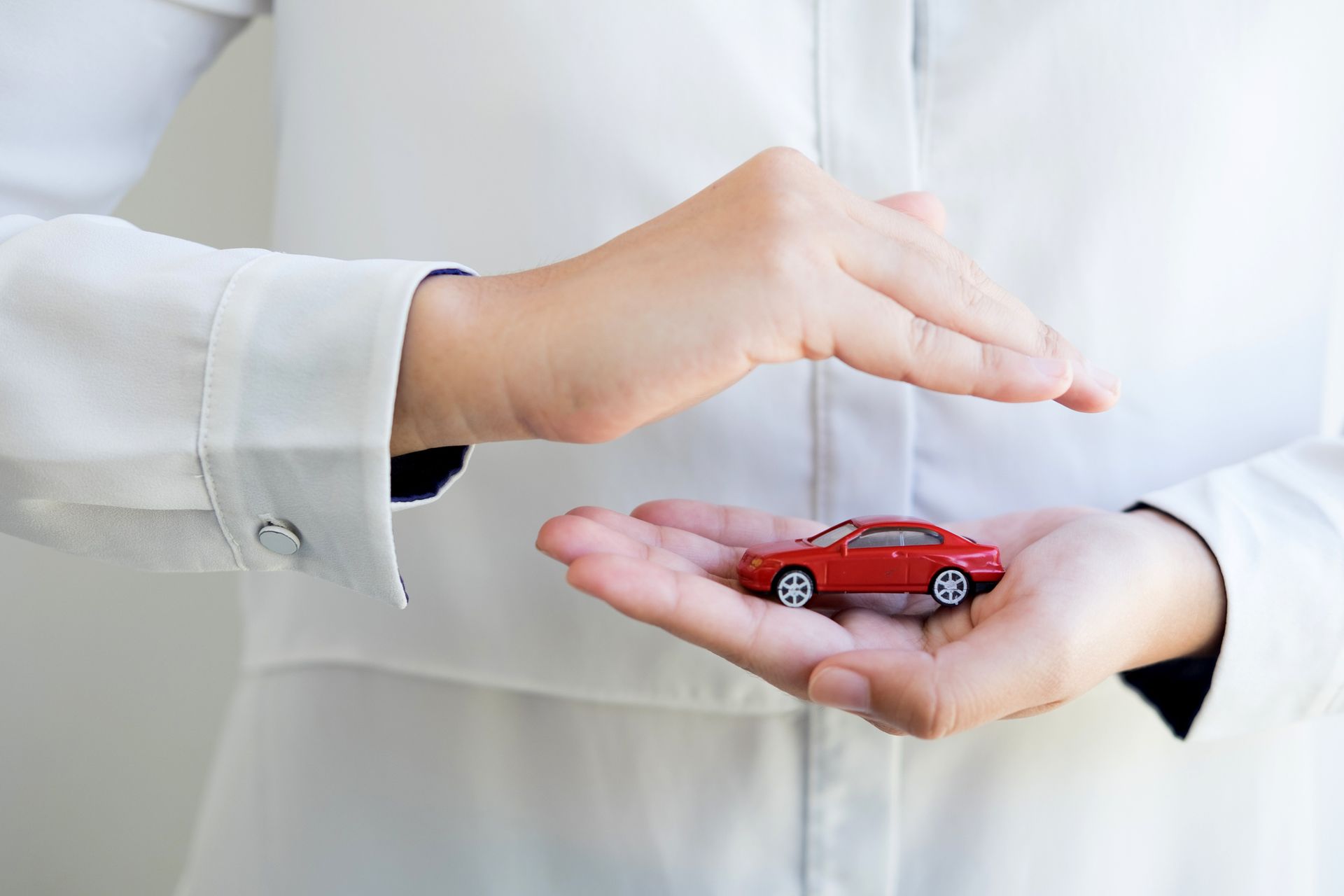 A close-up of a woman holding a red toy car, symbolizing a car insurance agency.