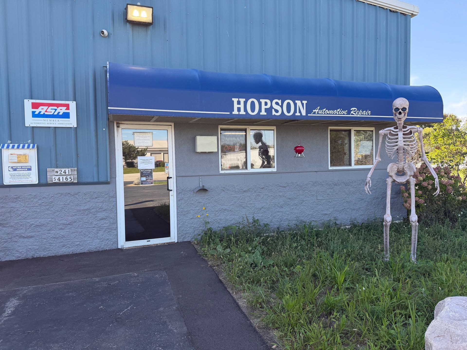 Hopson Auto Repair exterior with blue awning, skeleton decoration, gray building, and glass door. | Hopson Automotive