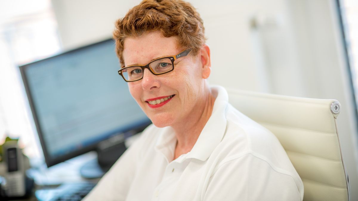 Eine Frau mit Brille sitzt an einem Schreibtisch vor einem Computer.
