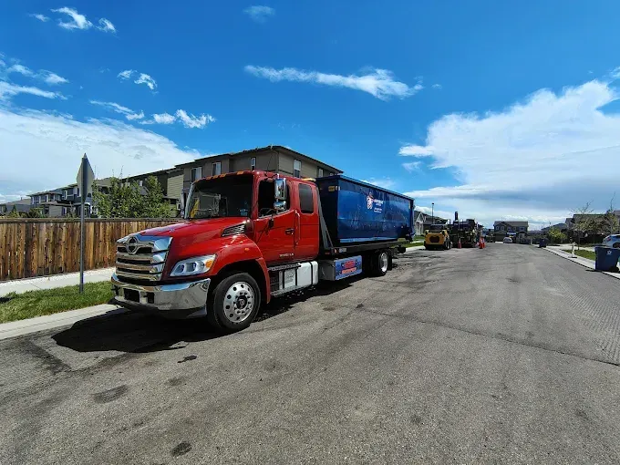 Red and blue dump truck parked on street, blue sky with clouds.