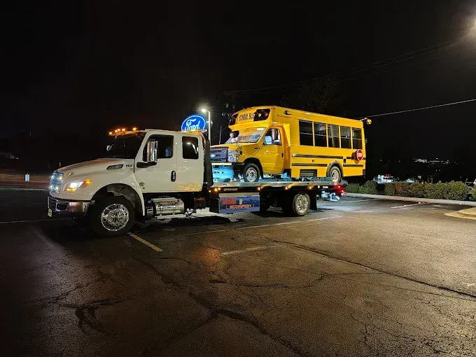 A small yellow school bus on a flatbed tow truck at night.