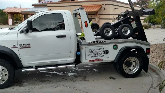 White tow truck parked; flatbed, black tow arm, and wheels visible.