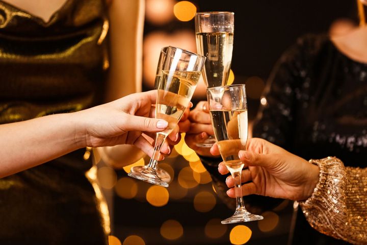 Mani che alzano calici di champagne in un brindisi celebrativo contro luci calde e sfocate.