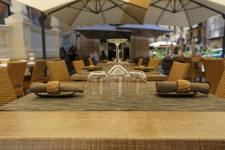 Terrazza esterna del ristorante con tavoli ben apparecchiati, ombrelloni beige e sedie in vimini.